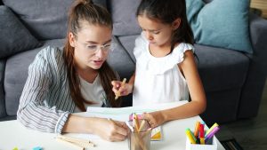 Happy family daughter and mother drawing picture at table in apartment, joyful kid is smiling enjoying hobby and mother's help. People and lifestyle concept.
